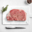 Load image into Gallery viewer, Petrusco Caviar fresh Japanese A5 Wagyu Striploin Steak on a marble cutting board with herbs, fresh pepper, and salt.