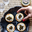 Load image into Gallery viewer, petrusco hybrid river beluga caviar on cracker with spread on black plate with hand reaching