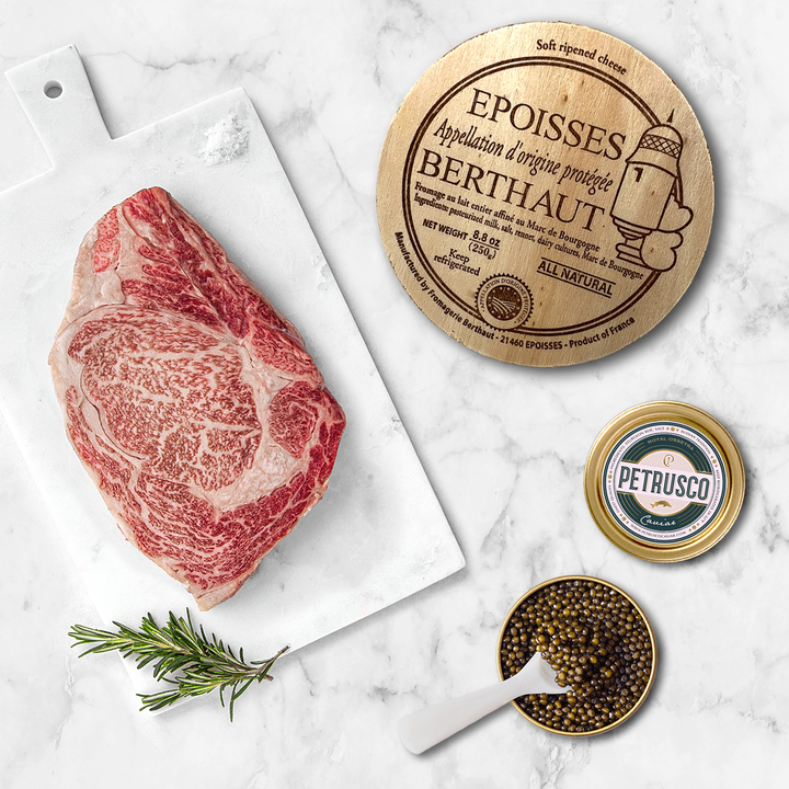 Petrusco Royal Ossetra caviar, Wagyu steak, and Epoisses cheese sit side by side on a marble surface.