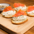 Load image into Gallery viewer, Smoked salmon and cream cheese canapés on a wooden cutting board.

