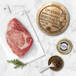 Load image into Gallery viewer, Flat lay of A5 Wagyu ribeye steak on a marble cutting board with rosemary, Berthaut Époisses AOP cheese, and an open Petrusco caviar tin with mother-of-pearl spoon.

