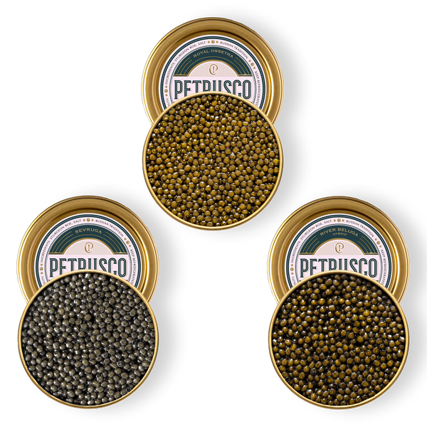 Three open gold tins of Petrusco caviar — golden-green Royal Ossetra, dark gray Sevruga, and olive-green River Beluga Hybrid — viewed from above.