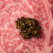 Load image into Gallery viewer, Close-up of glistening olive-green caviar pearls resting on richly marbled raw A5 Wagyu beef.
