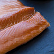 Load image into Gallery viewer, Close-up of golden smoked rainbow trout fillets on a dark slate surface showing rich amber color and delicate texture.
