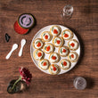 Load image into Gallery viewer, Overhead view of blini topped with crème fraîche, smoked trout roe, and dill on a white plate, with Petrusco tin, mother-of-pearl spoons, pink flower, and vodka glasses.
