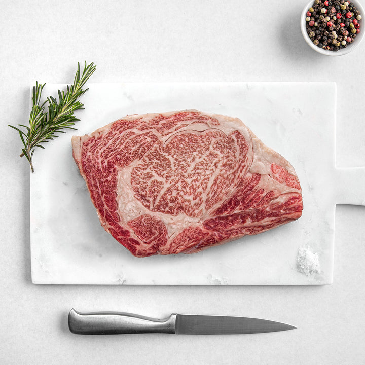 Petrusco Caviar fresh Japanese A5 Wagyu Ribeye Steak on a marble cutting board with herbs, fresh pepper, and salt.